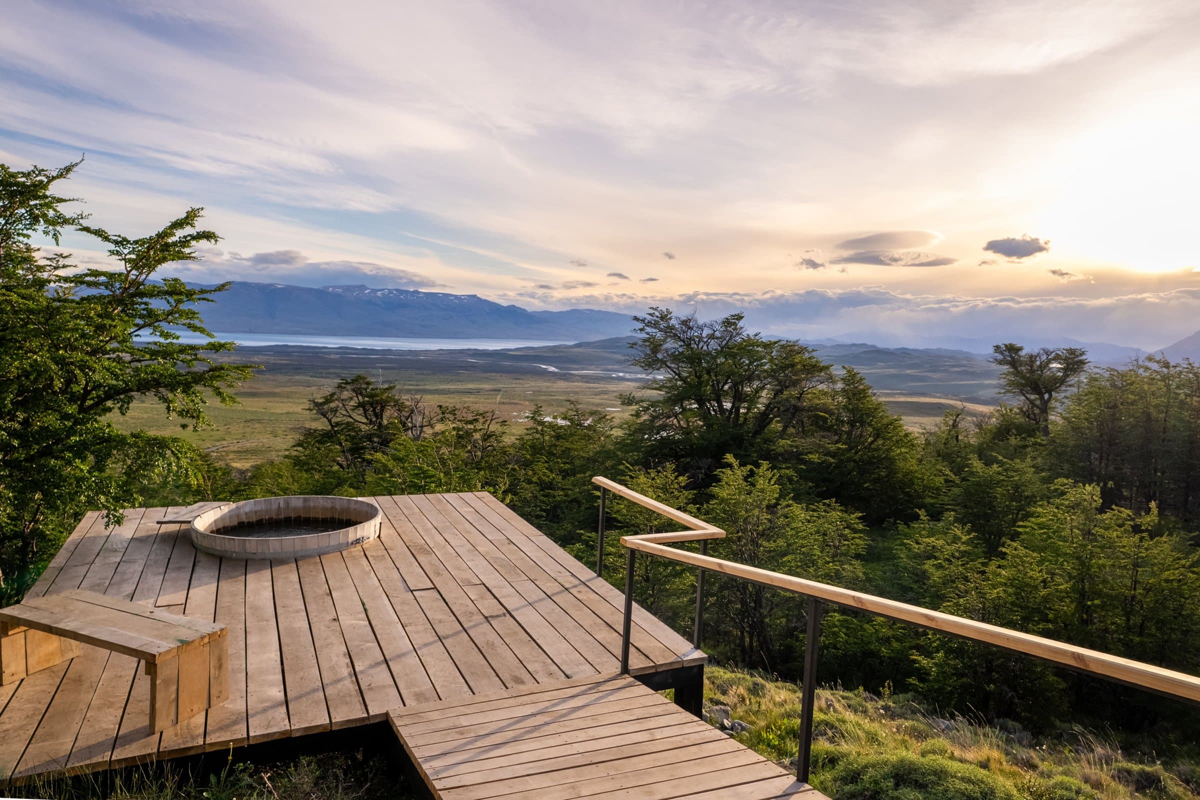 A lodge deck with a hot tub overlooking a valley in Patagonia at sunset
